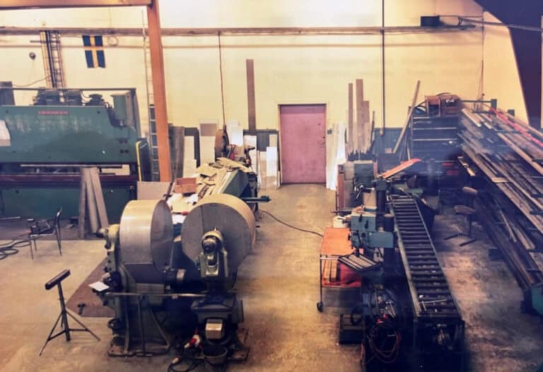 Äldre industrilokal på Almhaga gård där produktion av rostfria filter påbörjades under slutet av 1980-talet, med maskiner och material i en enkel verkstadsmiljö.